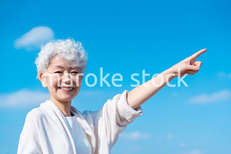 青空の下で未来を指差すシニアの女性