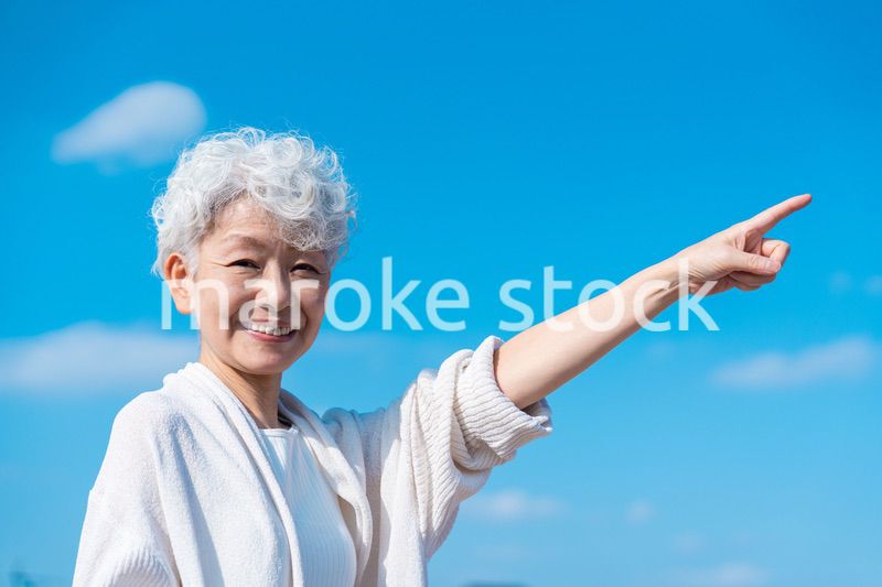 青空の下で未来を指差すシニアの女性