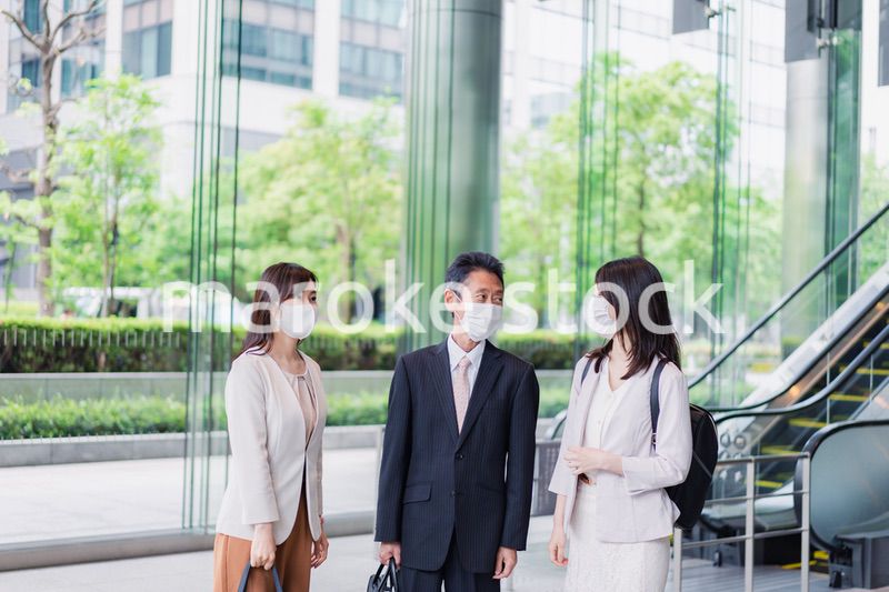 マスクをしてオフィスで立ち話をするビジネスパーソン