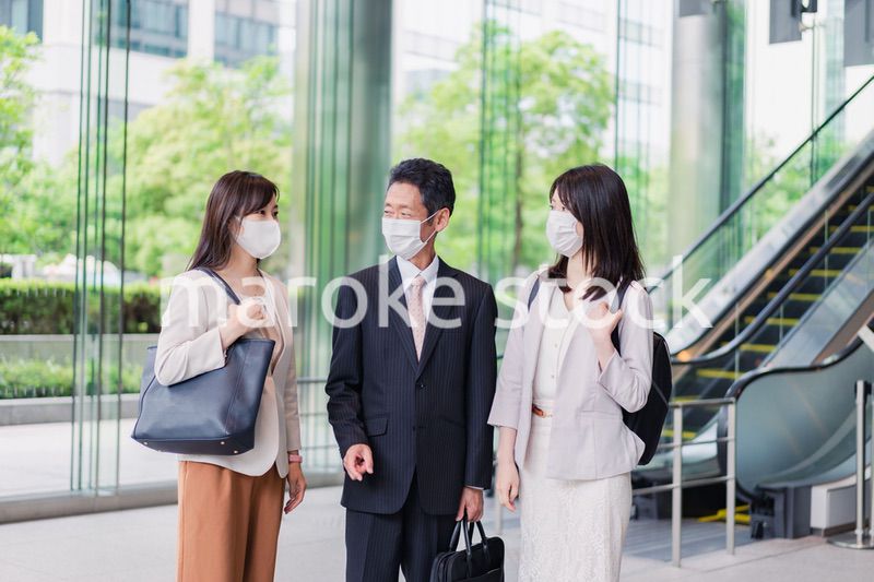 マスクをしてオフィスで立ち話をするビジネスパーソン