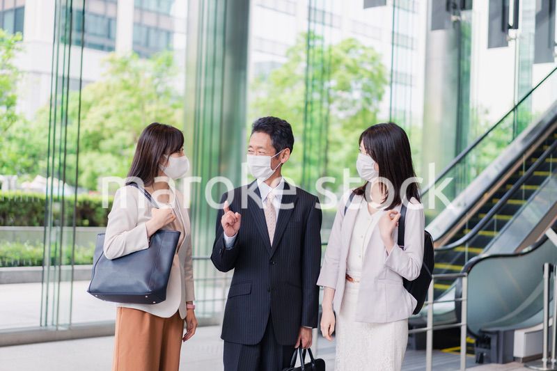 マスクをしてオフィスで立ち話をするビジネスパーソン