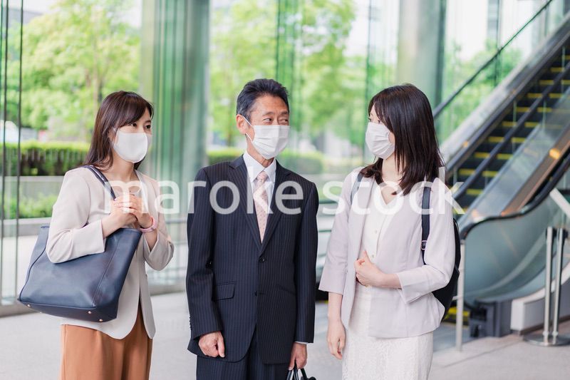 マスクをしてオフィスで立ち話をするビジネスパーソン