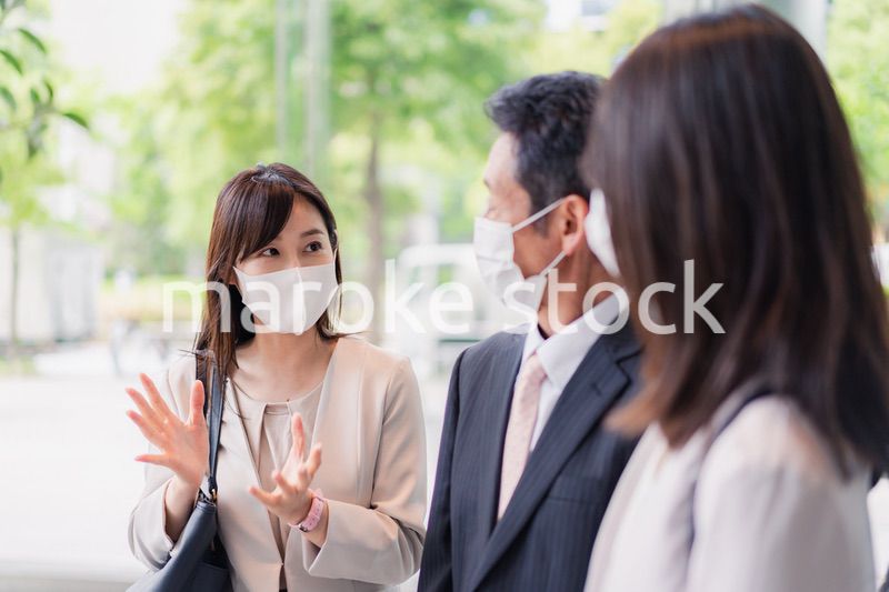 マスクをしてオフィスで立ち話をするビジネスパーソン
