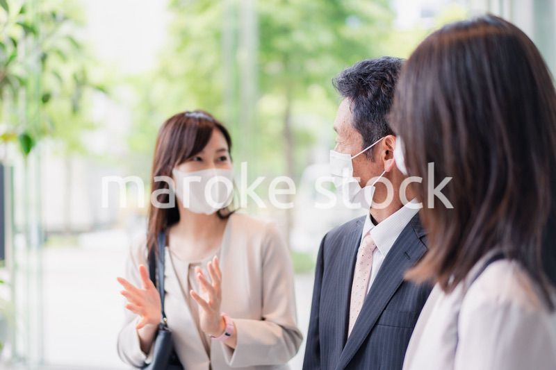 マスクをしてオフィスで立ち話をするビジネスパーソン