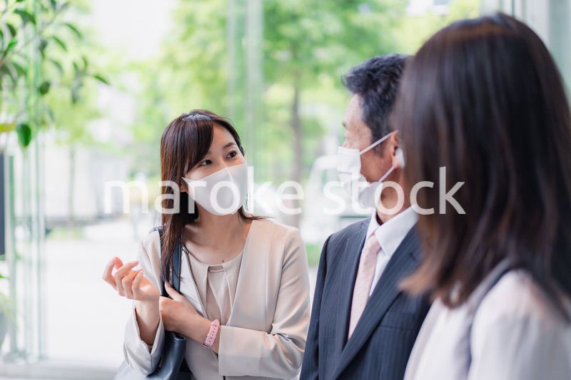 マスクをしてオフィスで立ち話をするビジネスパーソン