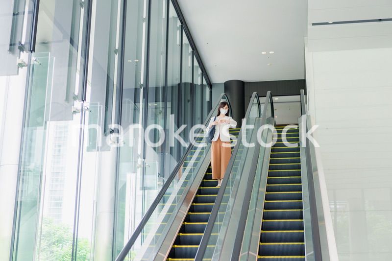 マスクをしてエスカレーターにのるビジネスウーマン