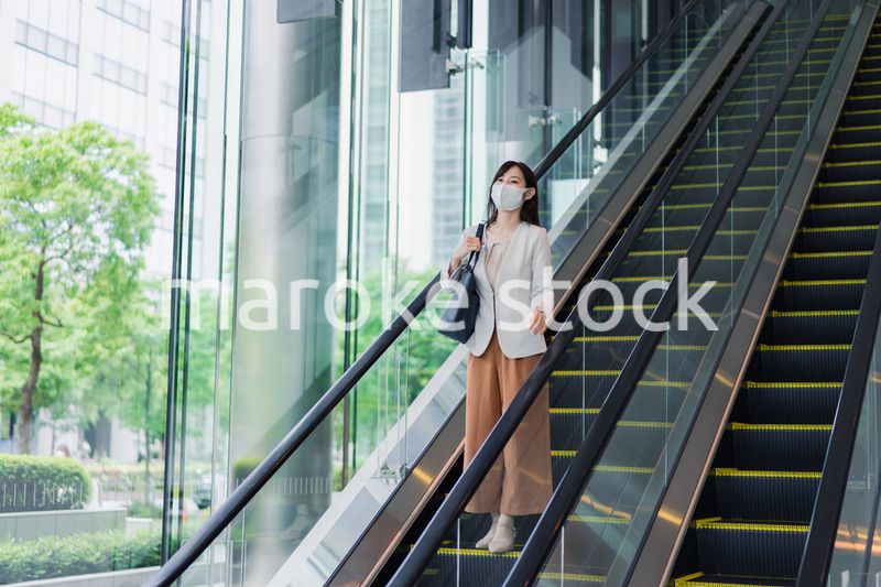マスクをしてエスカレーターにのるビジネスウーマン