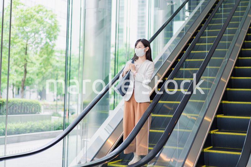 マスクをしてエスカレーターにのるビジネスウーマン