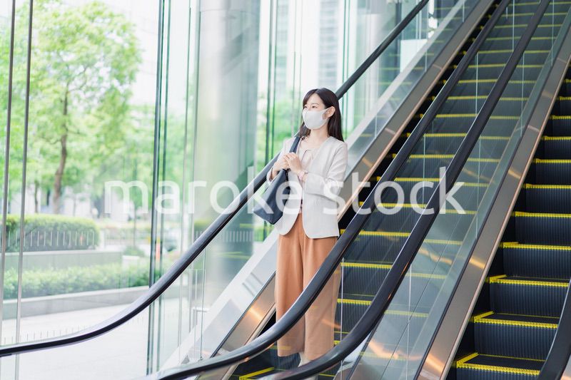 マスクをしてエスカレーターにのるビジネスウーマン
