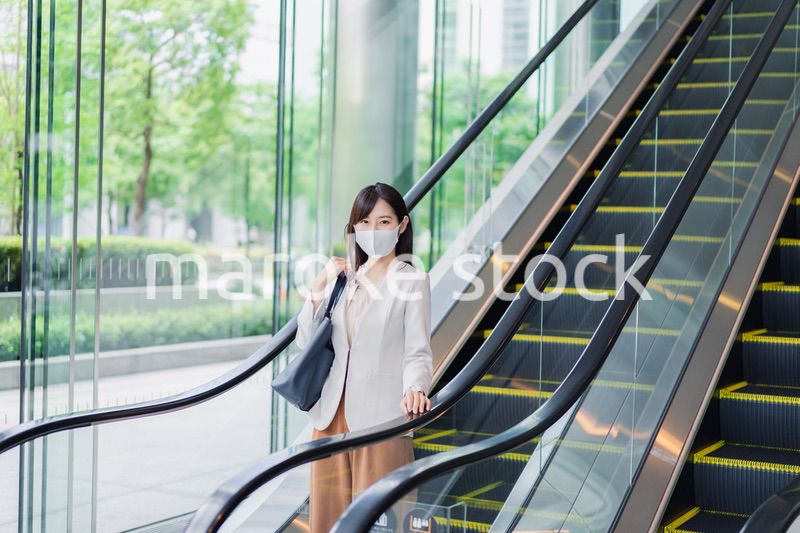 マスクをしてエスカレーターにのるビジネスウーマン