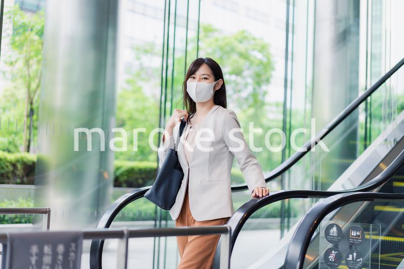 マスクをしてエスカレーターにのるビジネスウーマン