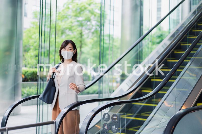 マスクをしてエスカレーターにのるビジネスウーマン
