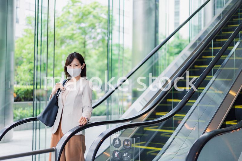 マスクをしてエスカレーターにのるビジネスウーマン