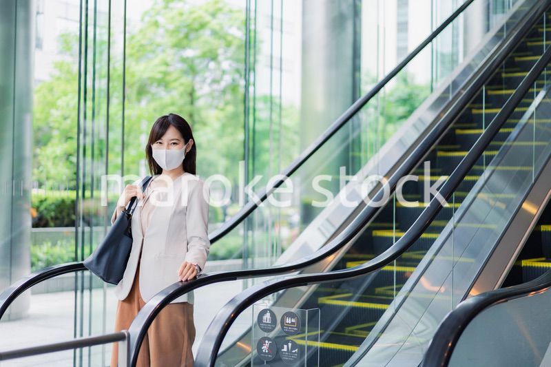 マスクをしてエスカレーターにのるビジネスウーマン