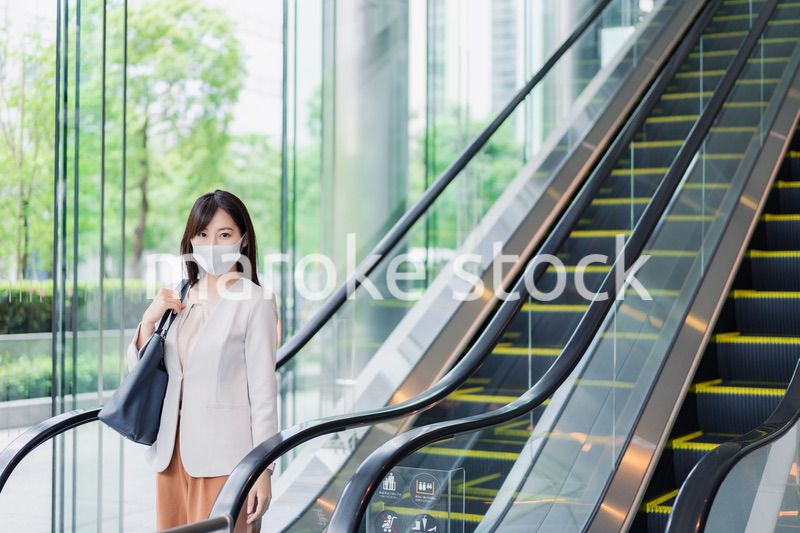 マスクをしてエスカレーターにのるビジネスウーマン