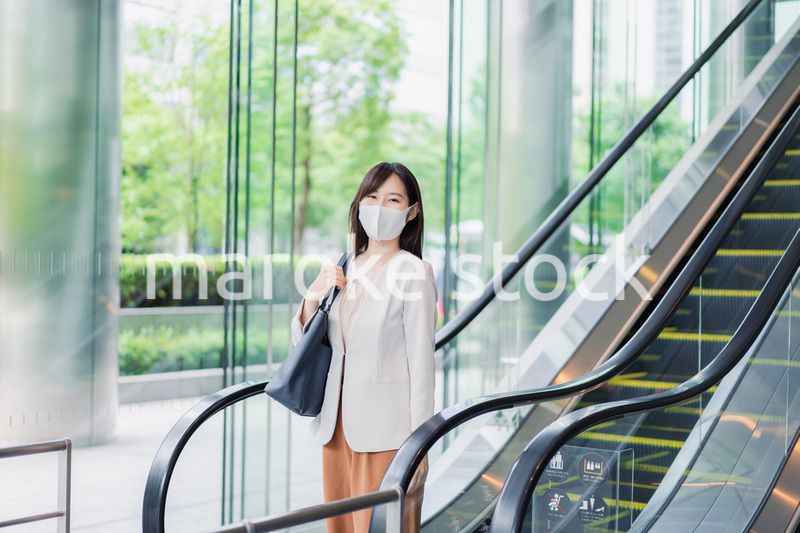 マスクをしてエスカレーターにのるビジネスウーマン
