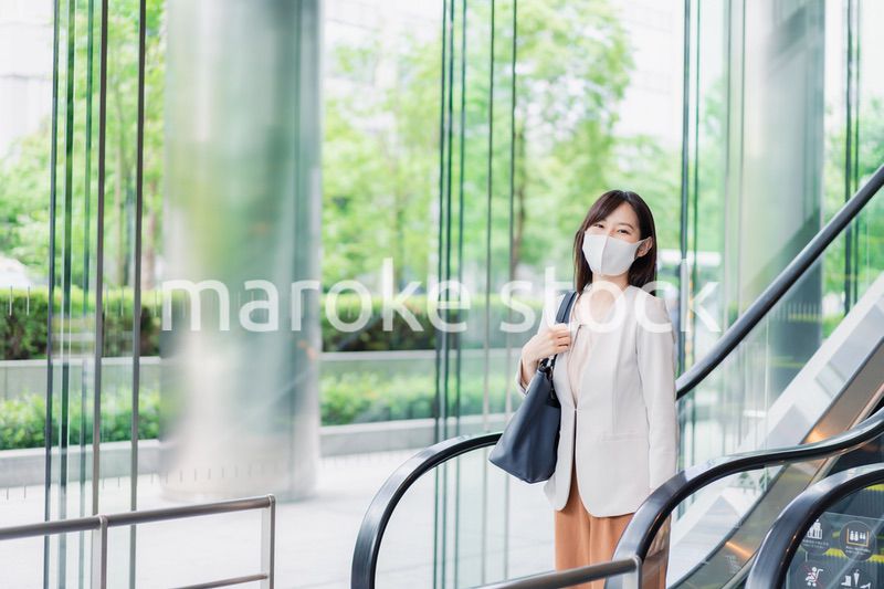 マスクをしてエスカレーターにのるビジネスウーマン