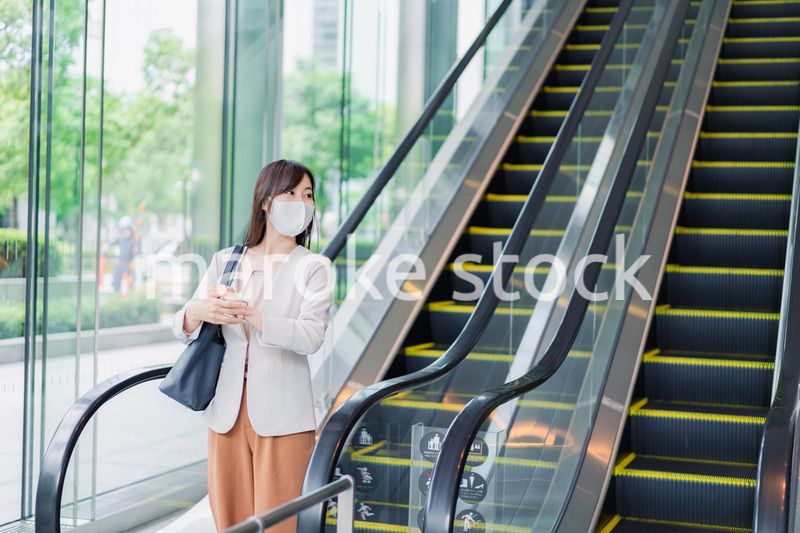 マスクをしてエスカレーターにのるビジネスウーマン