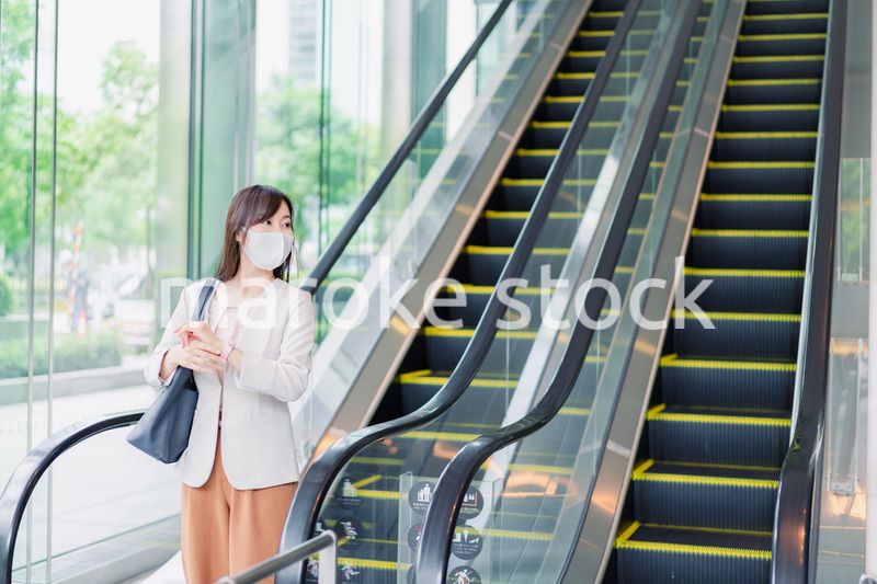 マスクをしてエスカレーターにのるビジネスウーマン
