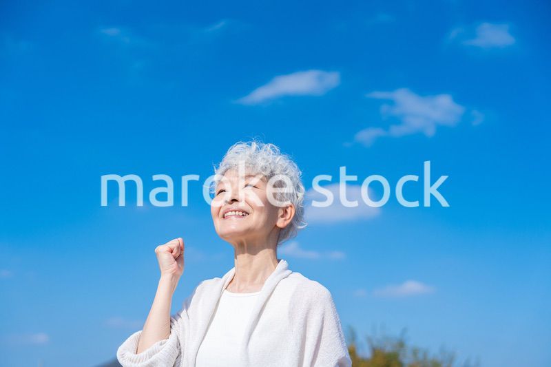 青空の下でガッツポーズをするシニアの女性
