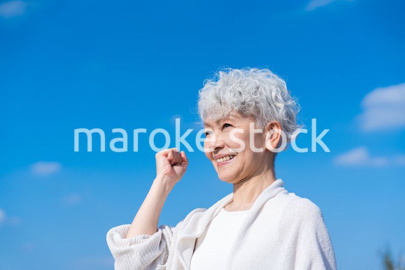 青空の下でガッツポーズをするシニアの女性
