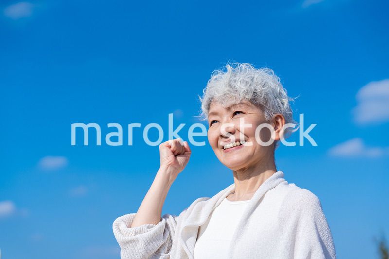 青空の下でガッツポーズをするシニアの女性