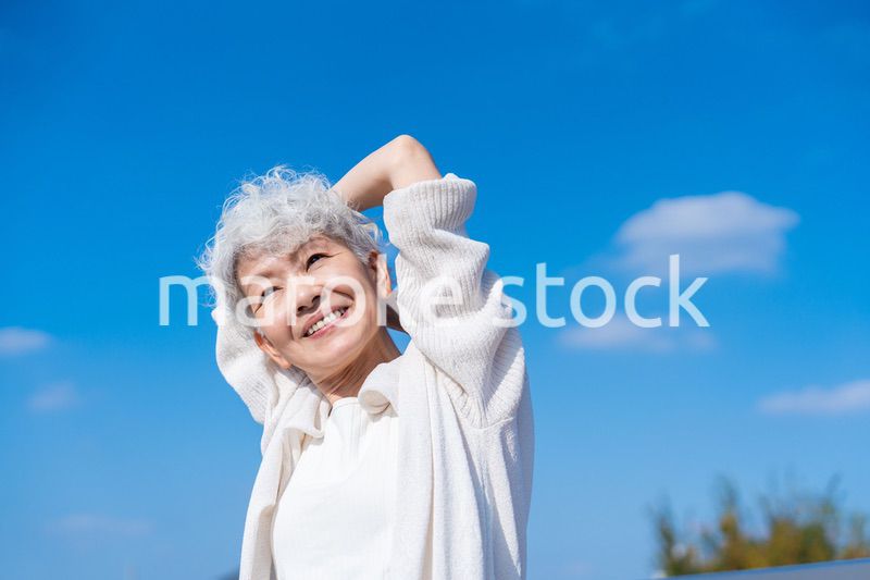 青空の下でストレッチをするシニアの女性