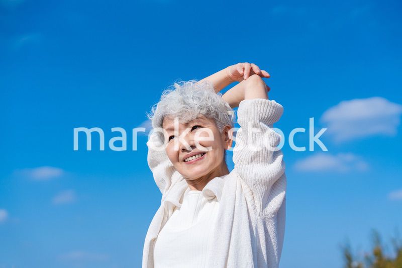 青空の下でストレッチをするシニアの女性