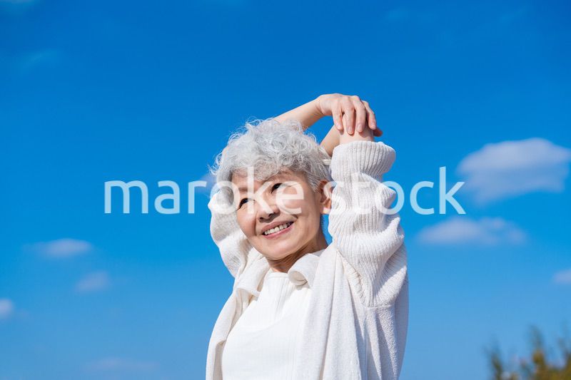 青空の下でストレッチをするシニアの女性
