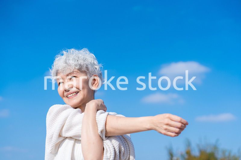 青空の下でストレッチをするシニアの女性