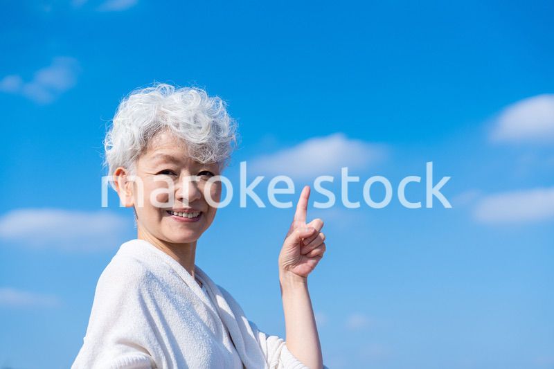 青空の下でオススメを指差すシニアの女性