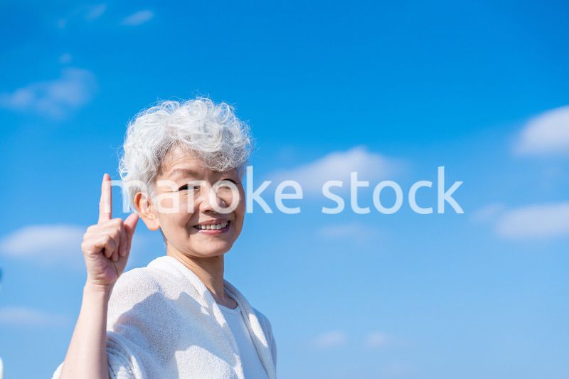 青空の下でオススメを指差すシニアの女性