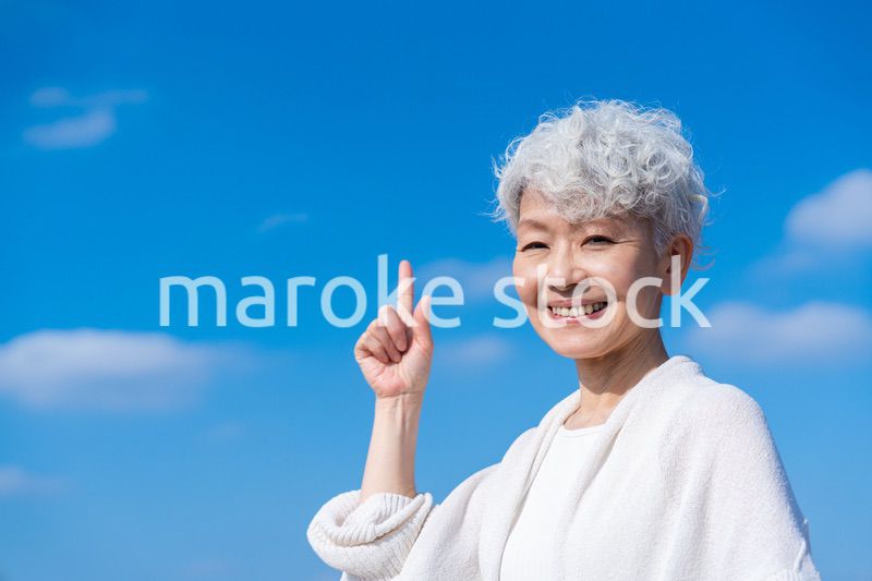 青空の下でオススメを指差すシニアの女性