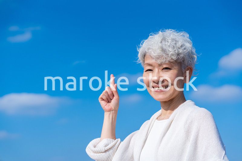 青空の下でオススメを指差すシニアの女性