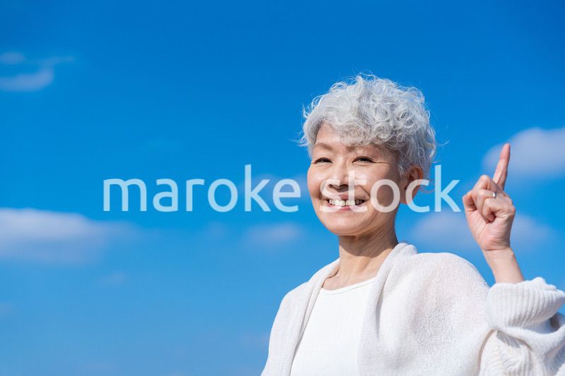 青空の下でオススメを指差すシニアの女性