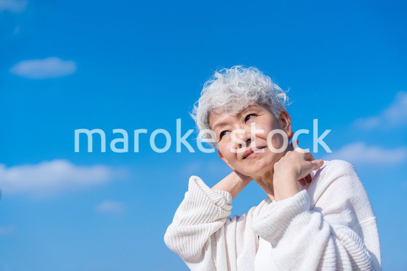 青空の下でストレッチをするシニアの女性