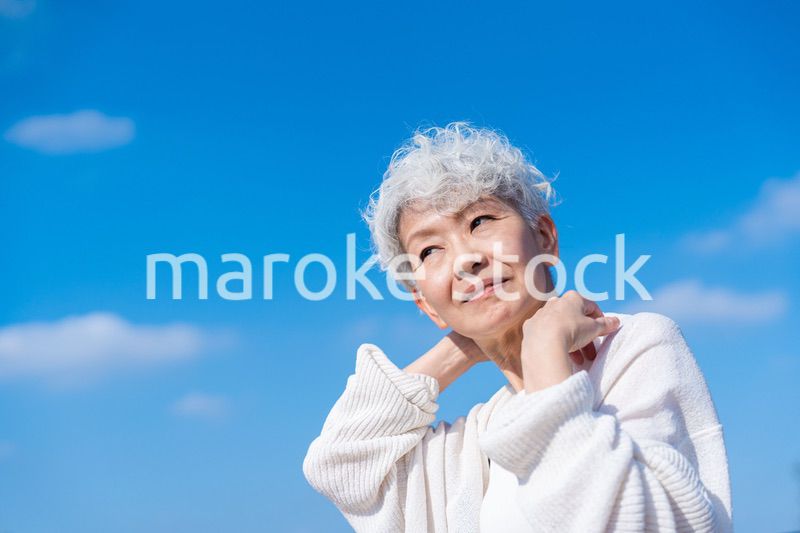 青空の下でストレッチをするシニアの女性