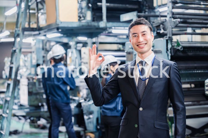 工場でOKサインをするビジネスマン