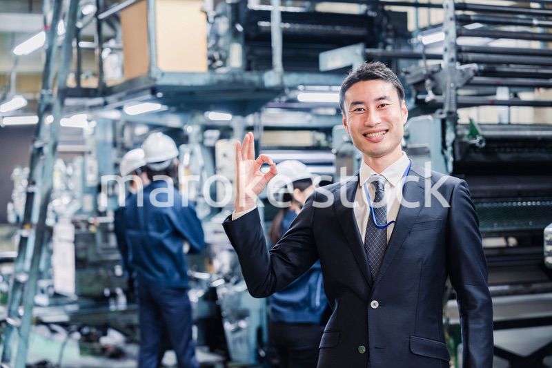 工場でOKサインをするビジネスマン