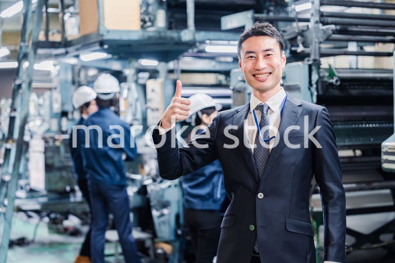 工場でOKサインをするビジネスマン