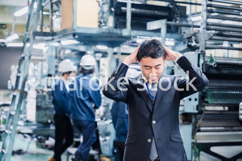 工場で頭を抱えるスーツの男性