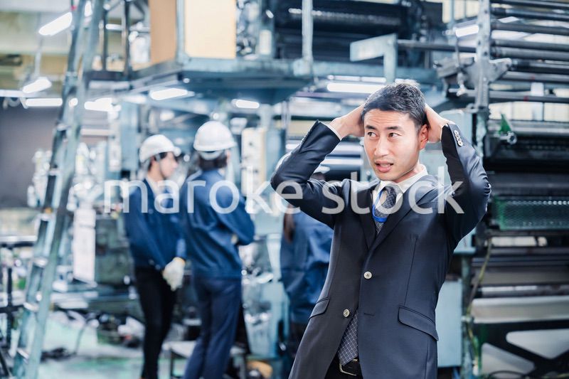 工場で頭を抱えるスーツの男性