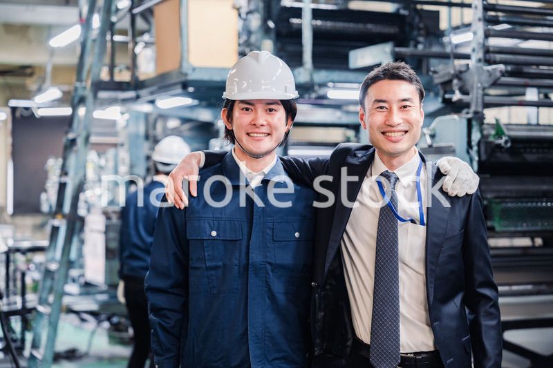 工場で肩を組む労働者と経営者