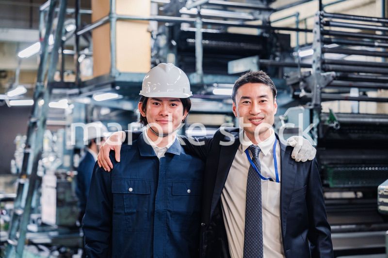 工場で肩を組む労働者と経営者