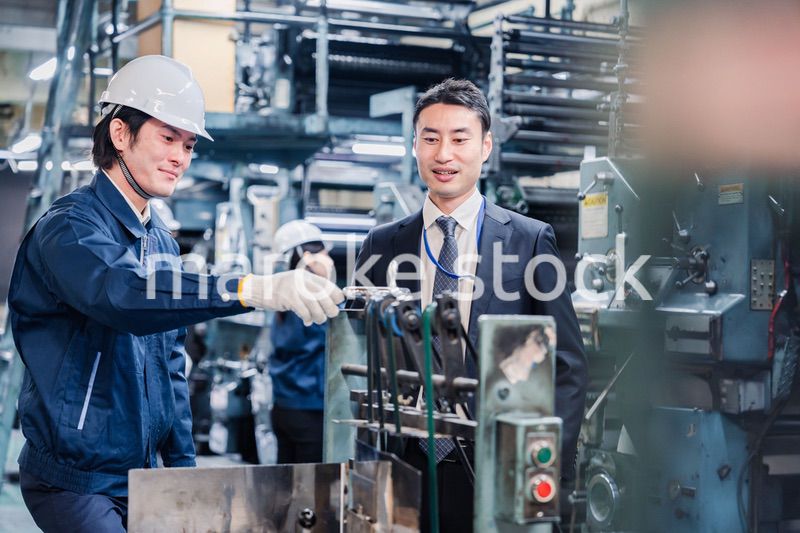 機械の前で話をする営業マンと労働者