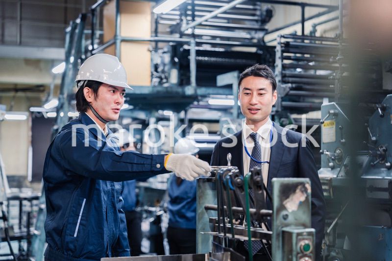 機械の前で話をする営業マンと労働者