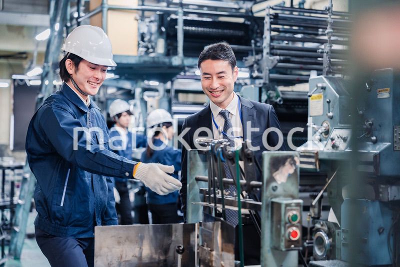 機械の前で話をする営業マンと労働者