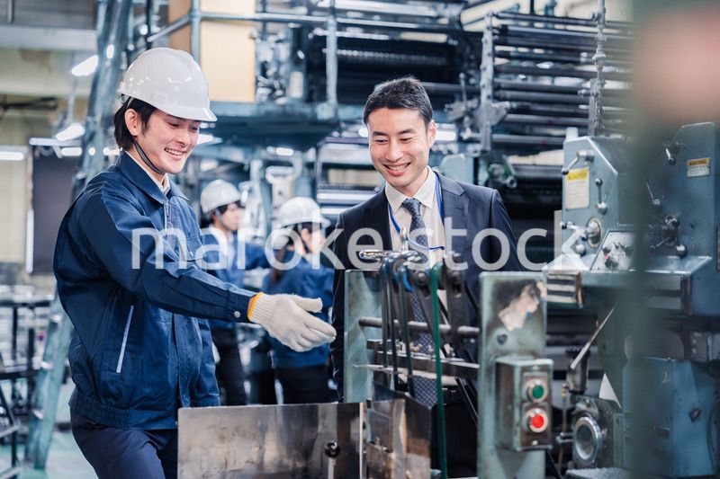 機械の前で話をする営業マンと労働者