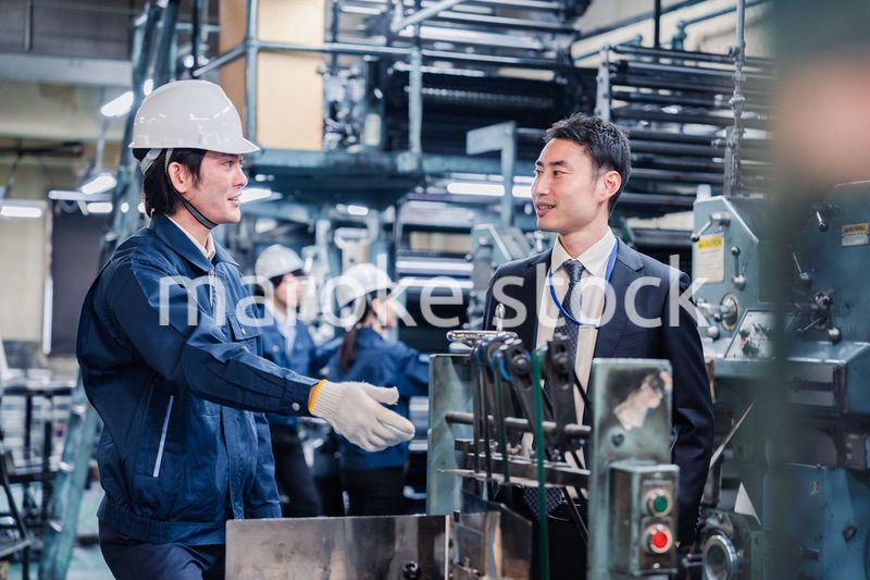 機械の前で話をする営業マンと労働者