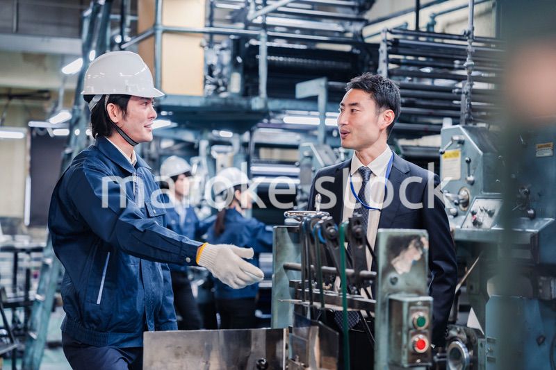 機械の前で話をする営業マンと労働者